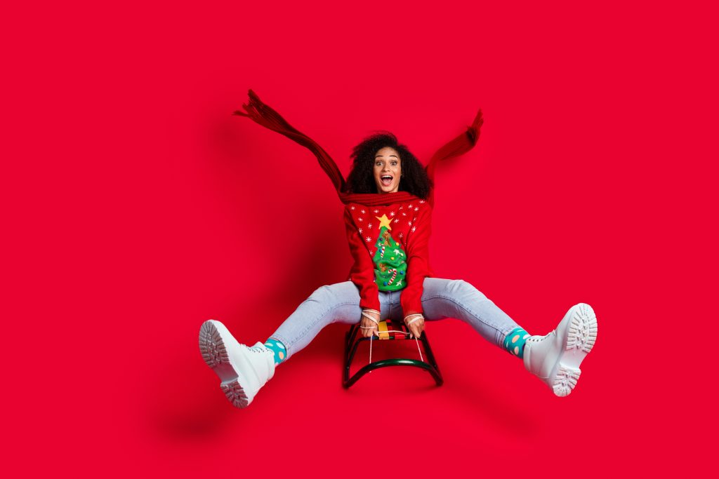 Photo of crazy funky cheerful girl wear ugly ornament sweater riding sleigh christmas festive event isolated on red color background.